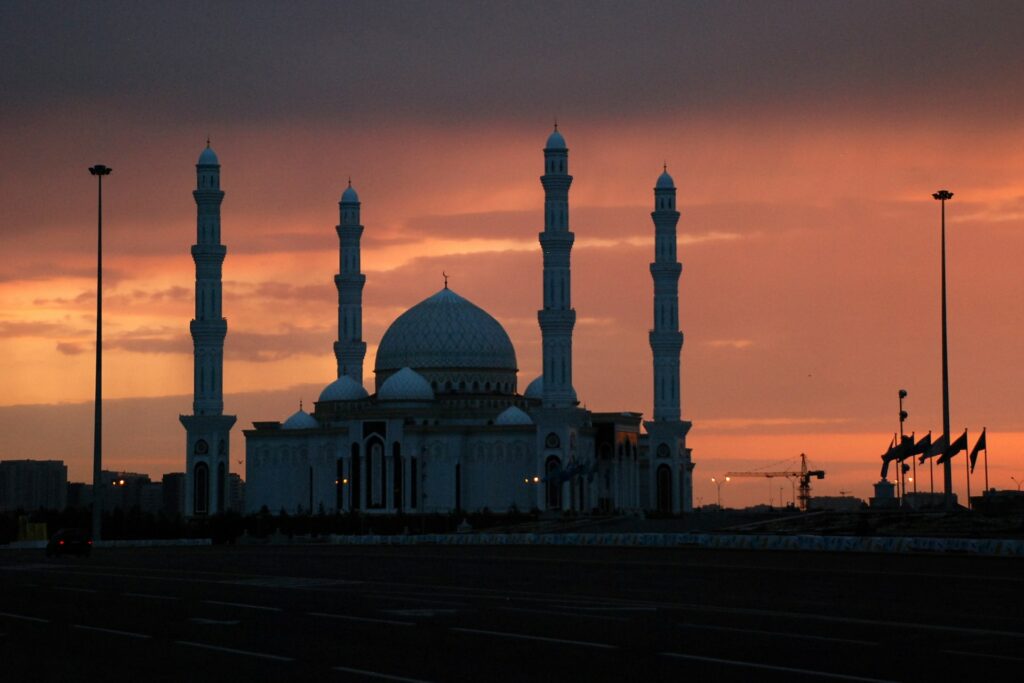 Uma mesquita com quatro torres e uma abóboda bem grande em um entardecer com o céu laranja