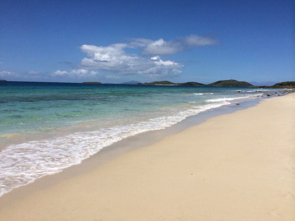 Uma praia com faixa de areia em bege claro com um mar em tom verde claro
