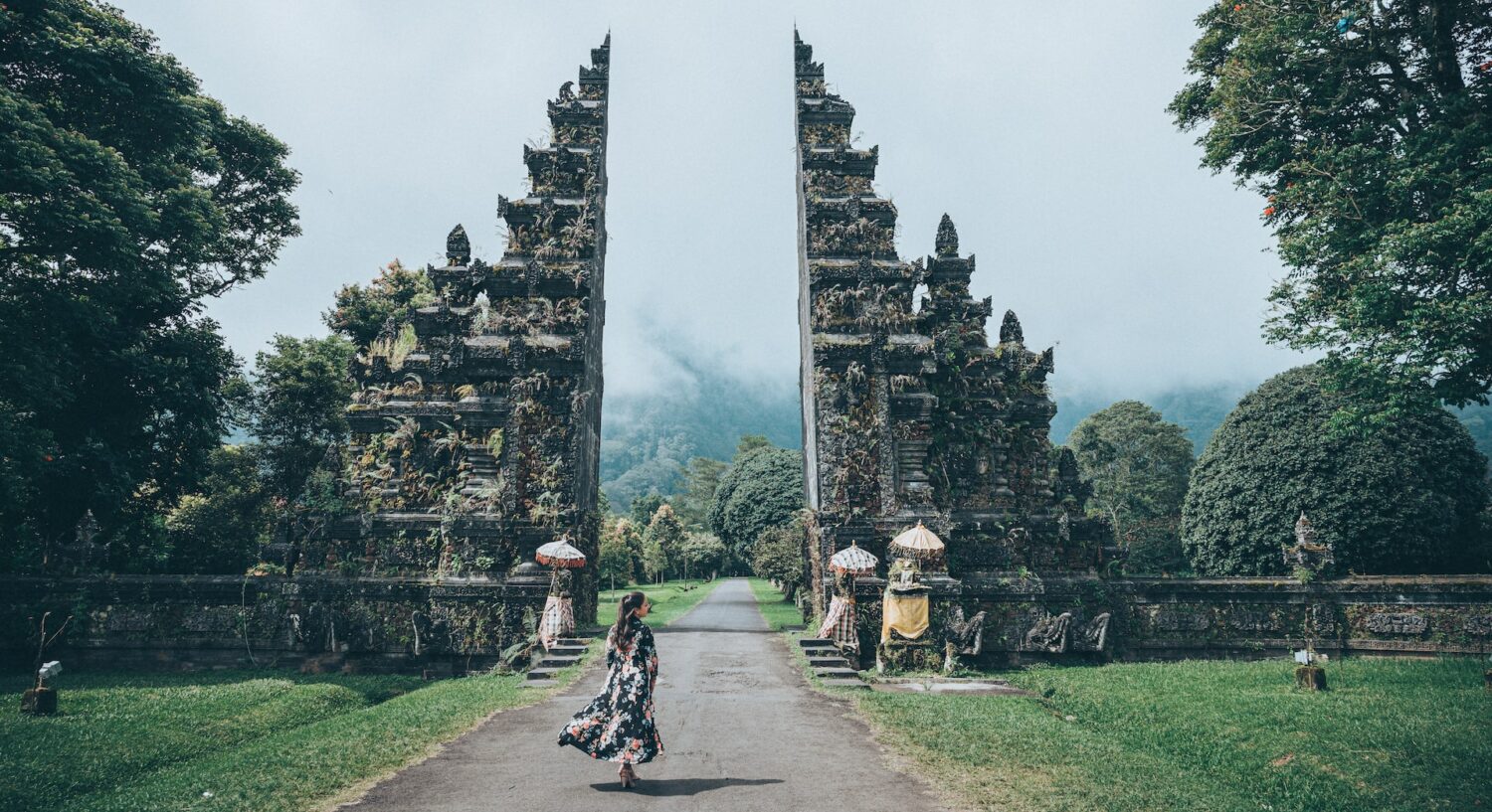 pessoa com roupas de tecidos esvoaçantes caminhando em direção a um portal de pedra ricamente trabalhado no Tempo Lempuyang, com grama verdinha ao redor, para ilustrar o post de chip celular Bali