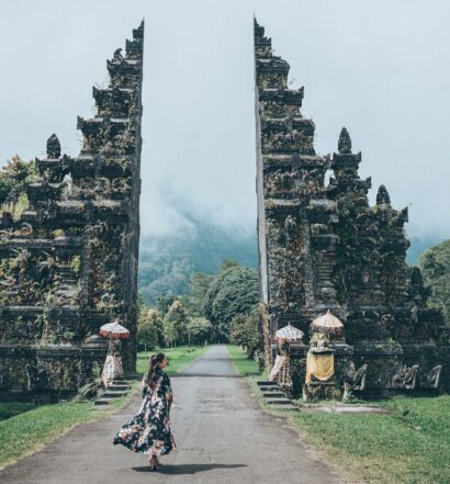 pessoa com roupas de tecidos esvoaçantes caminhando em direção a um portal de pedra ricamente trabalhado no Tempo Lempuyang, com grama verdinha ao redor, para ilustrar o post de chip celular Bali