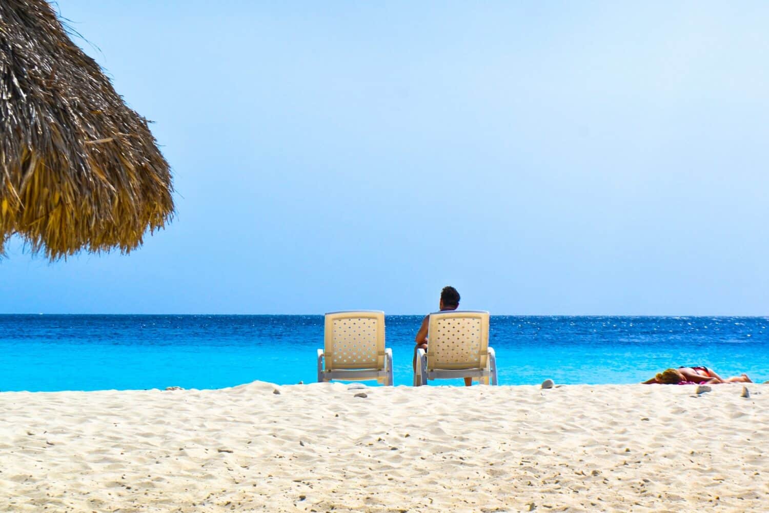 Um homem sentado em um cadeira de praia virada de frente para um mar muito azul