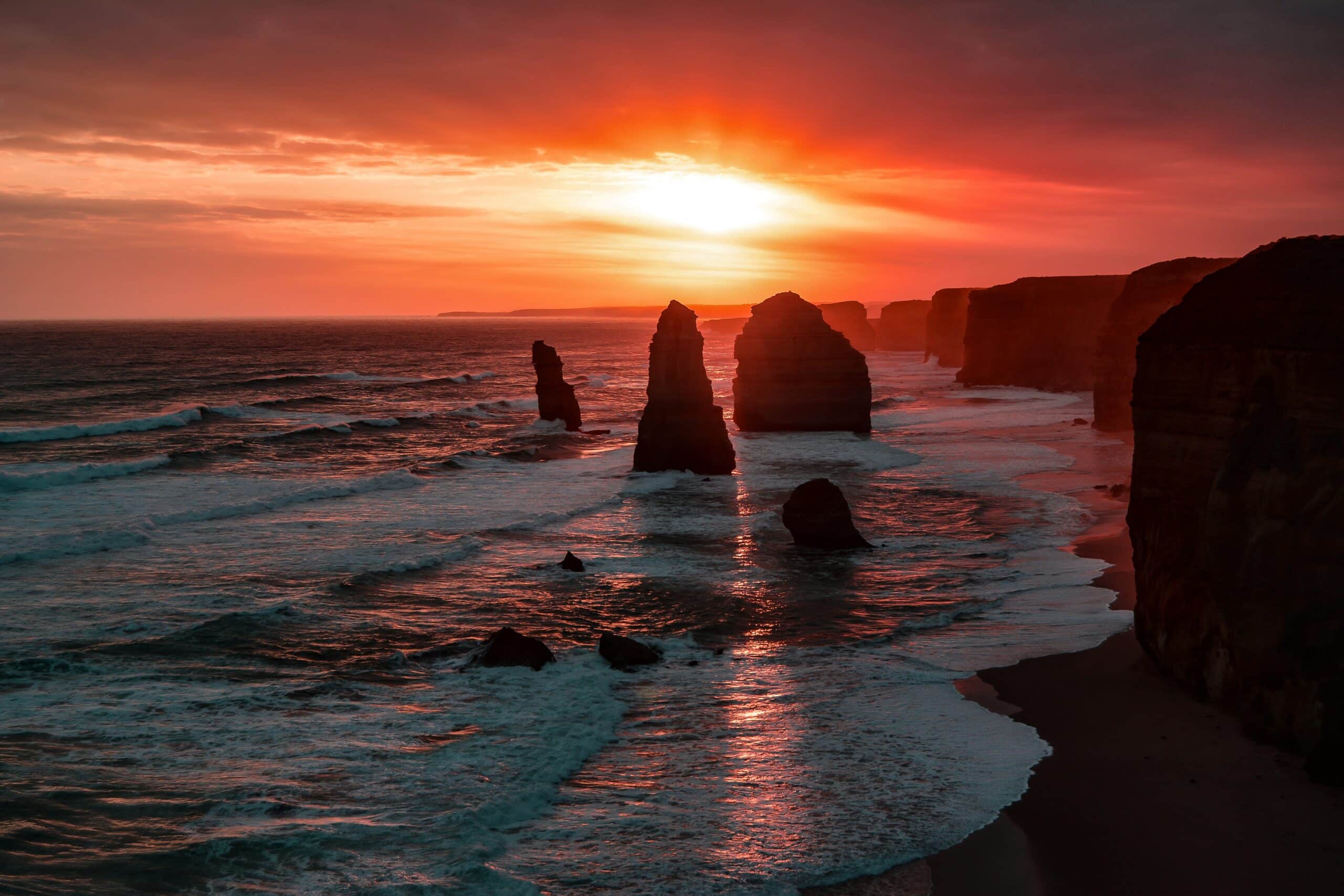 Pôr do sol no Twelve Apostles, Austrália, com mar batendo nas rochas.