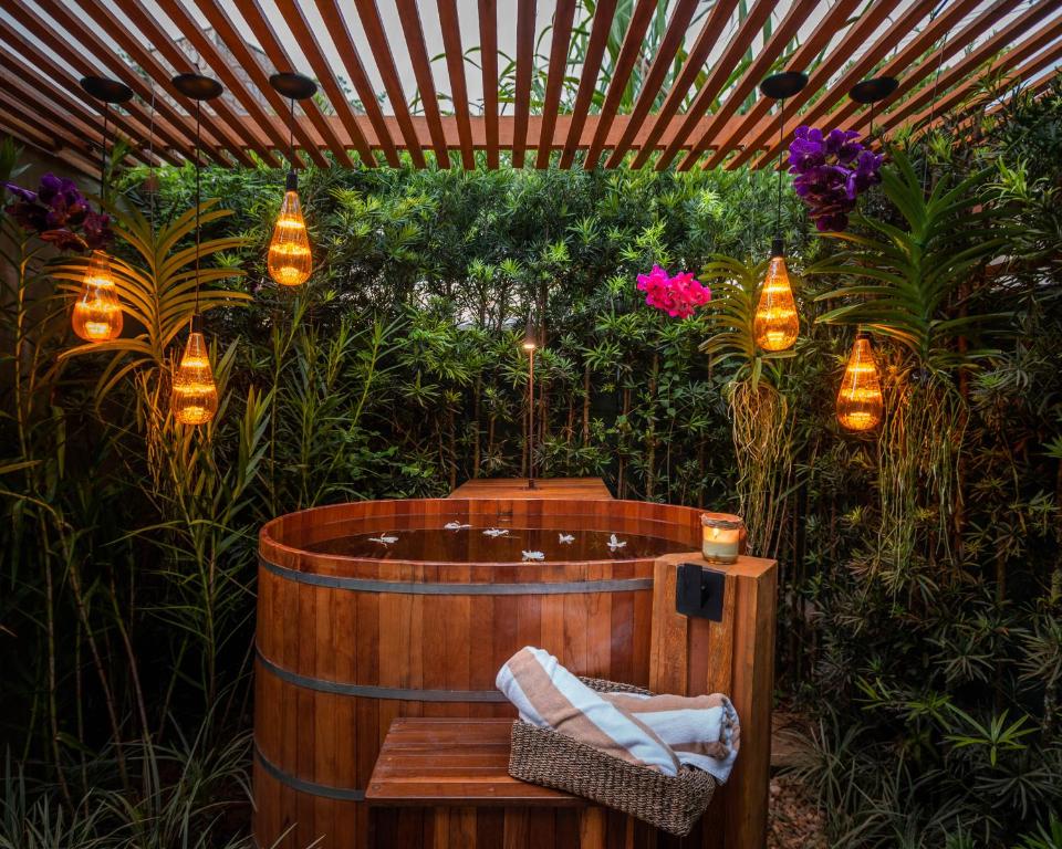 Banheira de hidromassagem na Villa Sapê Pousada num jardim cercado por plantas e lustres rústicos, dentro da banheira há algumas flores e algumas toalhas penduradas