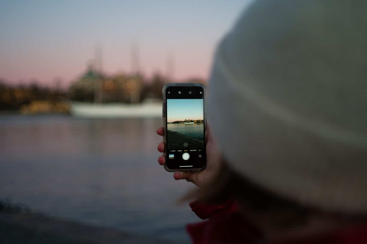 pessoa de costas com uma toca segurando um celular que dá vista para a baía da cidade, que ilustra o post de chip celular Estocolmo
