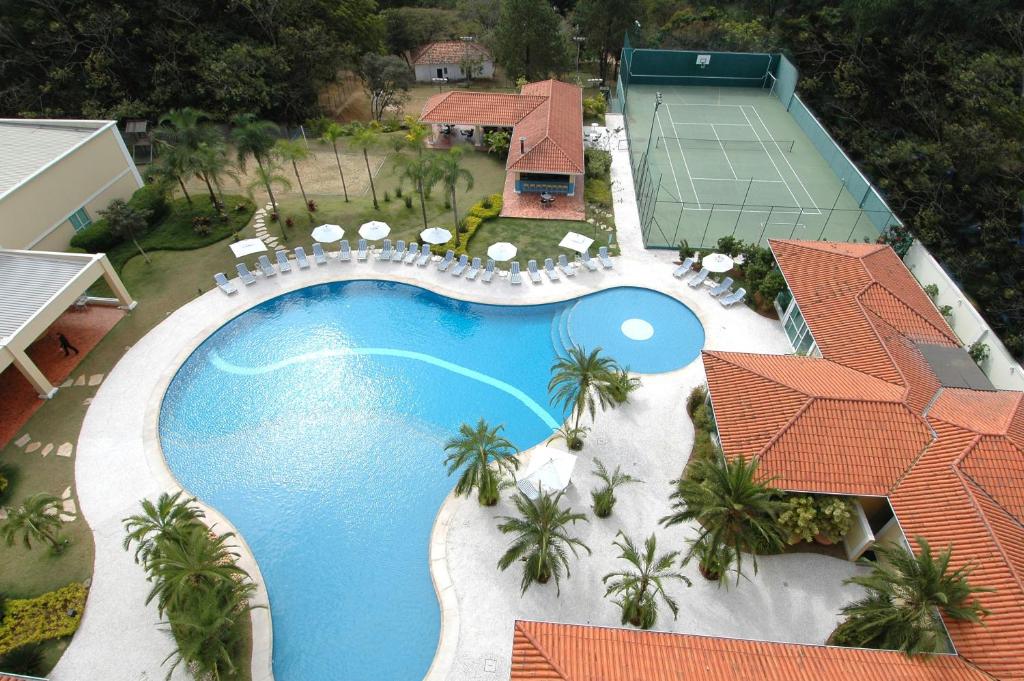 Vista aérea da piscina do Vitória Hotel Convention Indaiatuba com uma quadra de tênis perto, algumas espreguiçadeiras e coqueiros, para representar hotéis perto do Aeroporto de Viracopos em Campinas