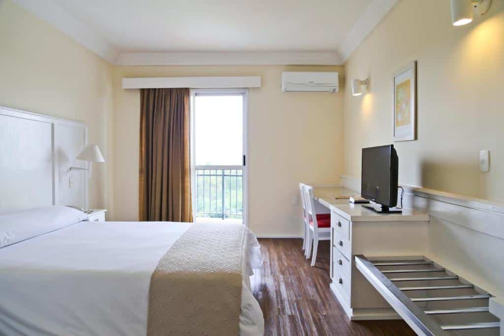 Quarto do Vitória Hotel Convention Indaiatuba com uma varanda, uma cama de casal, uma mesa de escritório com uma cadeira, um ar-condicionado, uma cômoda e uma televisão
