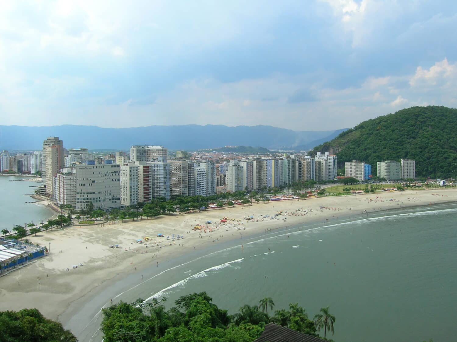 Orla de uma praia com muitos prédios e uma extensa faixa de areia, para representar hotéis em Santos