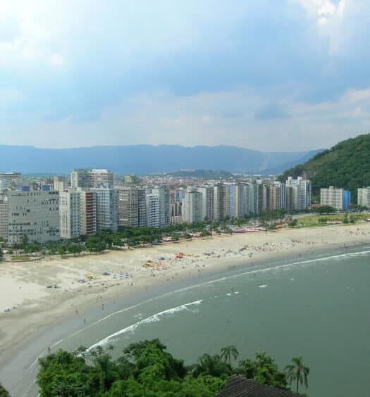 Orla de uma praia com muitos prédios e uma extensa faixa de areia, para representar hotéis em Santos