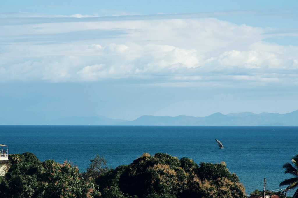 vista da praia de Nosy Be com águas bem azuis e céu azul claro com muitas nuvens e um barquinho ao longe, e muita vegetação abaixo, para ilustrar o post de chip celular Madagascar