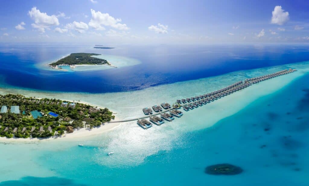 Vista aérea da ilha Baa Atoll, com um mar cristalino em volta e alguns chalés flutuantes no mar. Imagem para ilustrar o post de hotéis nas Maldivas