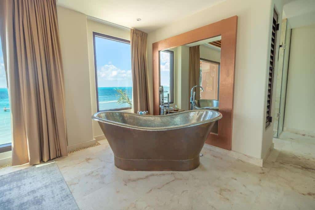 Banheira no  Hotel Beló Isla Mujeres em um cômoda com amplas janelas de frente para o mar, o chão é de mármore e há um grande espelho também