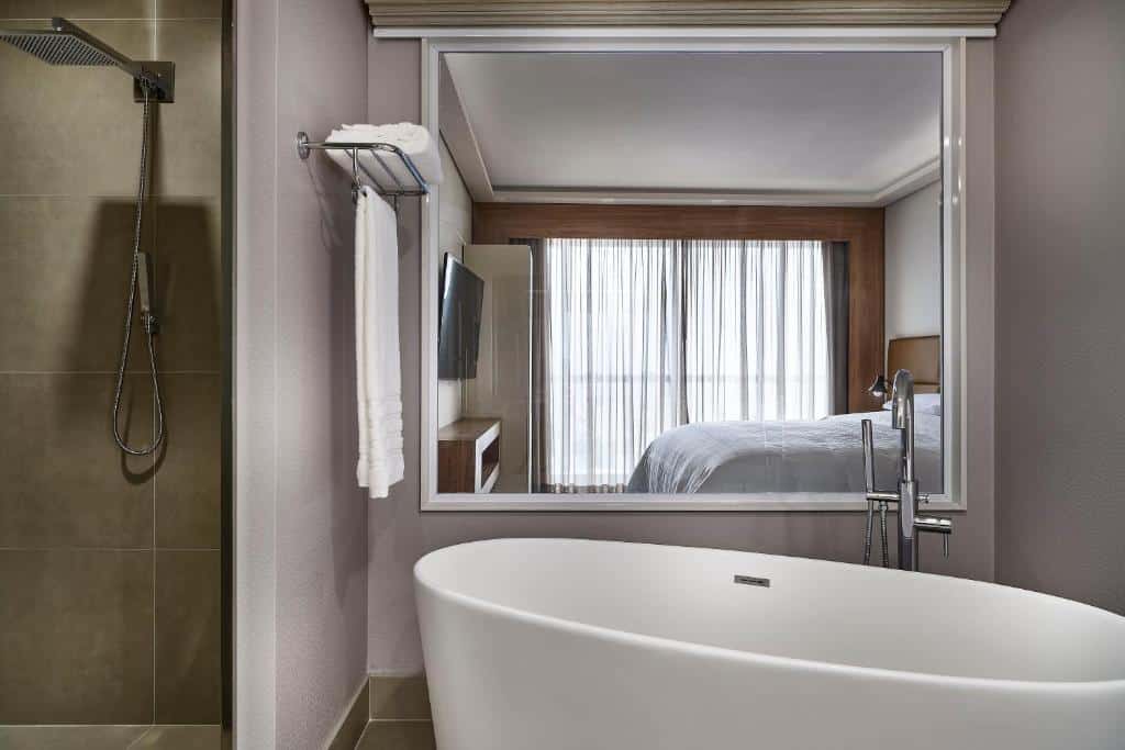 Banheira do Sheraton Santos Hotel com um amplo espelho, uma banheira em formato oval e algumas toalhas brancas ao lado