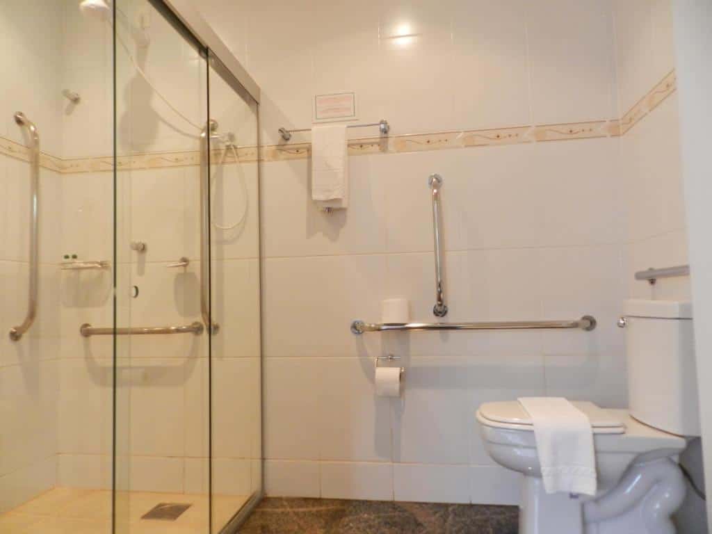 Banheiro do Holambra Garden Hotel  com barra de segurança perto do vaso sanitário e barras de segurança no chuveiro.