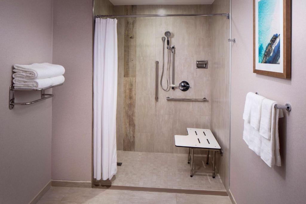 banheiro adaptado do Hyatt Place Aruba Airport mostrando o chuveiro com barras de apoio e um banquinho branco dentro do box.