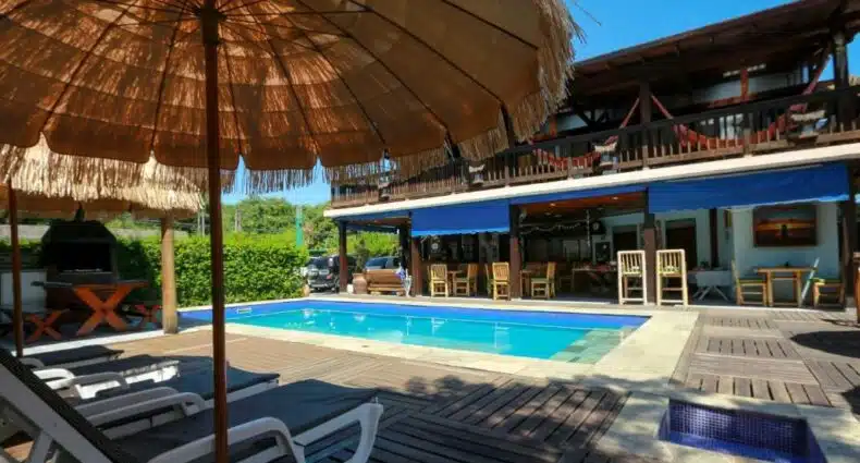 Vista da piscina durante o dia da Pousada Pura Vida Maresias com cadeira do lado direito e do lado esquerdo a hospedagem. Imagem para ilustrar o post pousadas na Praia do Engenho