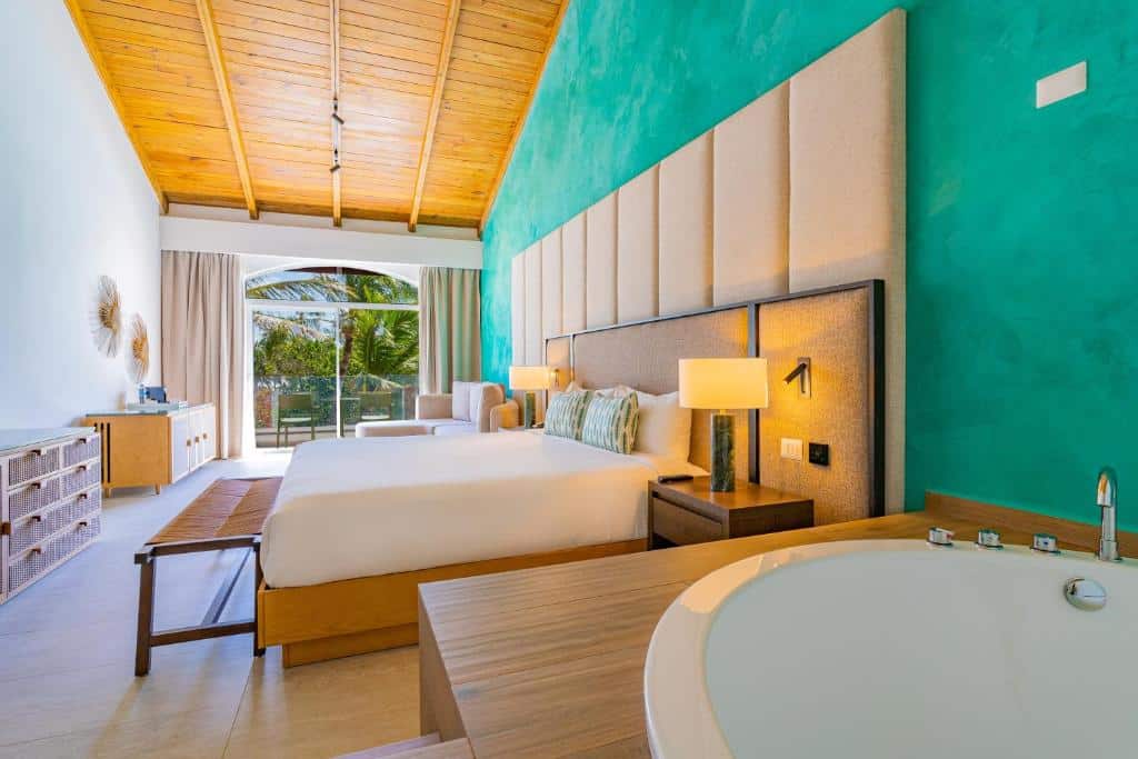 Suíte lua de mel do Caribe Deluxe, de 33 m², com hidro, cama de casal, área de estar com sofá e varanda com mesa e duas cadeiras. O quarto tem vista para a natureza, com árvores verdes. Imagem para ilustrar o post como escolher um resort em Punta Cana