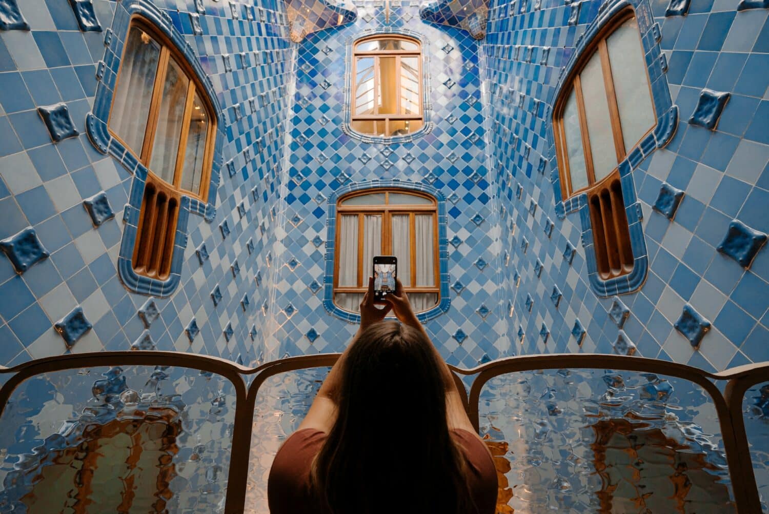 Mulher tirando foto com um celular da parede com azulejos azuis e janelas amarelas, ilustrando post chip celular Barcelona.