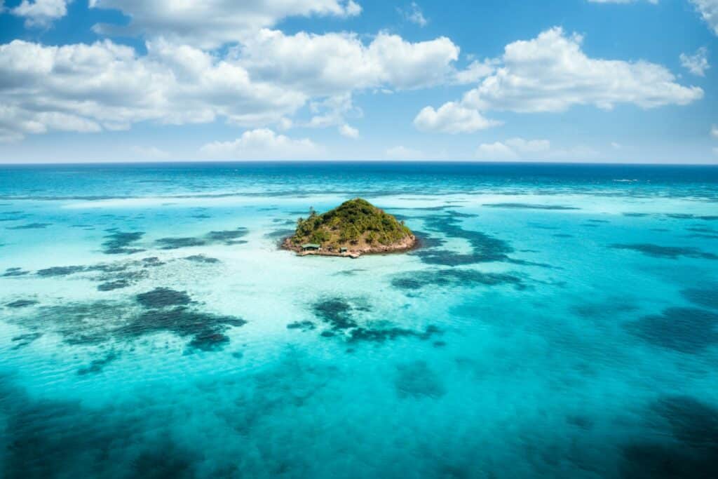 Ilhota chamada Cayo Cangrejo rodeada de um mar cristalino azul. A ilha tem bastante vegetação verde, durante um dia ensolarado com nuvens no céu