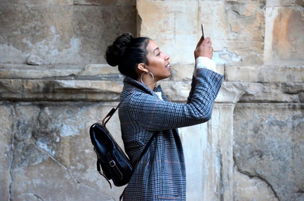 mulher segurando feliz um celular com uma parede de um prédio histórico ao fundo na França