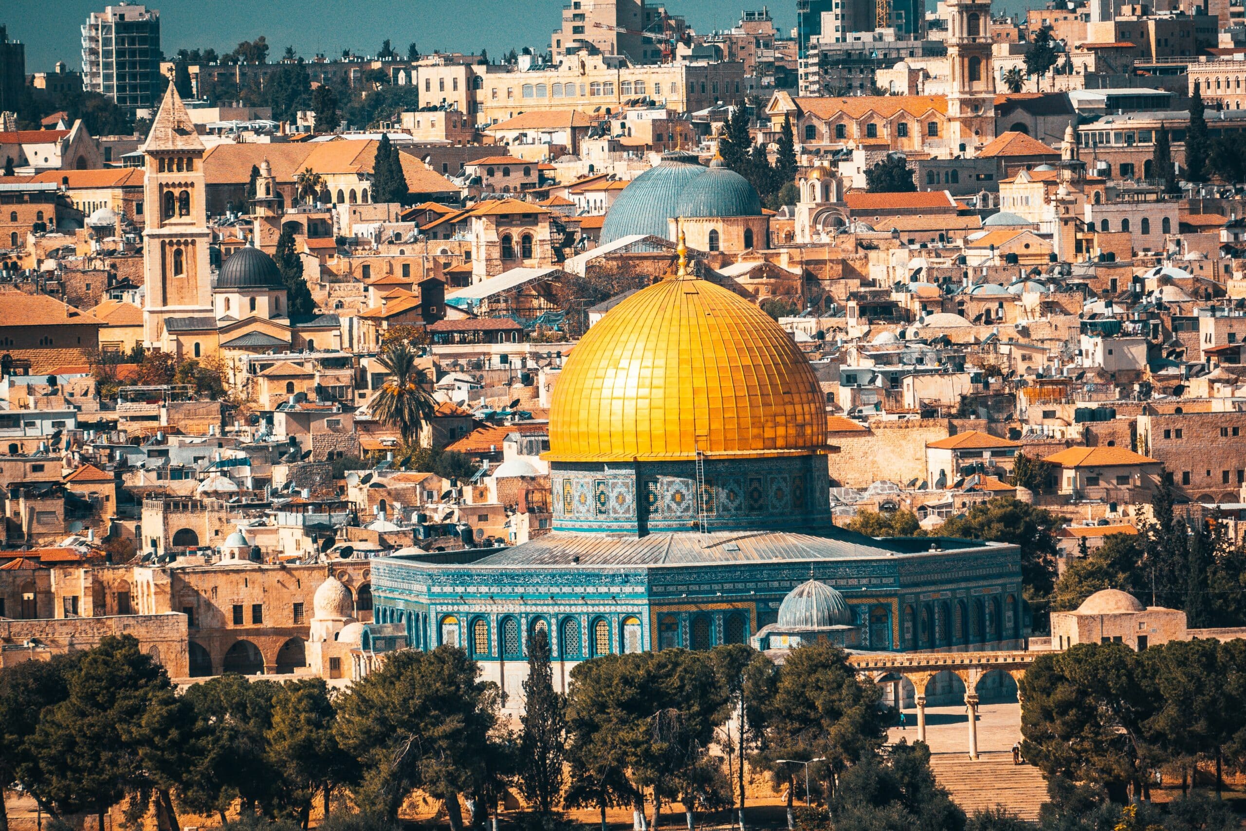 Vista da cidade de Jerusalém, em Israel, durante o dia com várias casas em cores marrom e o Monte do Templo com paredes azuis com a cúpula dourada no meio. Representa chip celular Jerusalém.