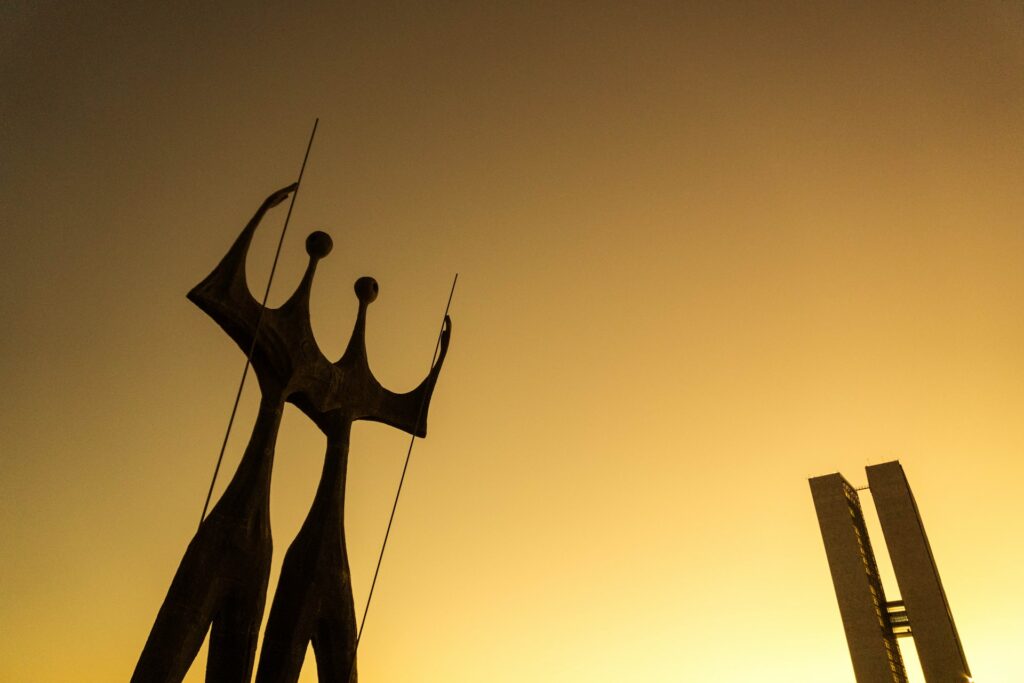 Duas estátuas altas uma do lado da outra fazendo a silhueta de duas pessoas muito magras com um dos braços erguidos