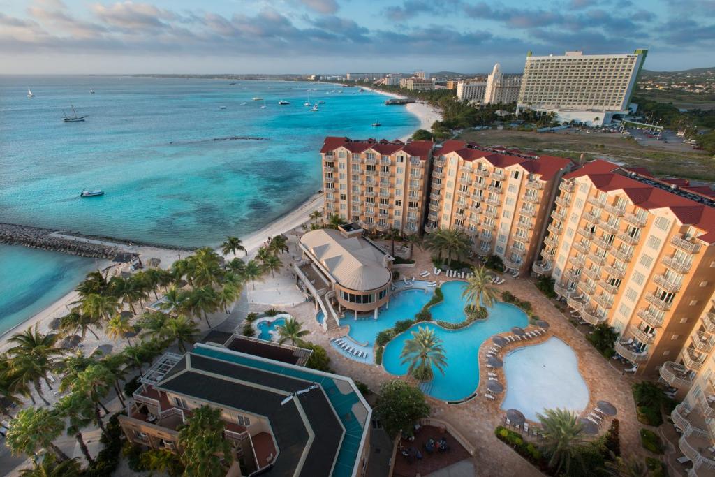 vista aérea do Divi Aruba Phoenix Beach Resort com o mar à esquerda e a praia com os resorts à direita, sendo que no canto inferior direito é possível enxergar a área de piscina e três prédios do hotel ao redor