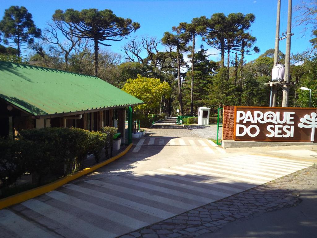 Vista da entrada do Parque do SESI Canela  com uma placa enorme com o nome do chalé ao fundo várias árvores. Representa chalés em Canela.