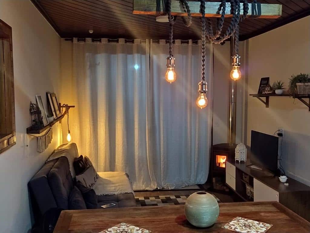 Sala de estar da hospedagem doce lar - casa bougainville em Teresópolis com sofá, tv, lareira e mesa, ilustrando post pousadas em Teresópolis.