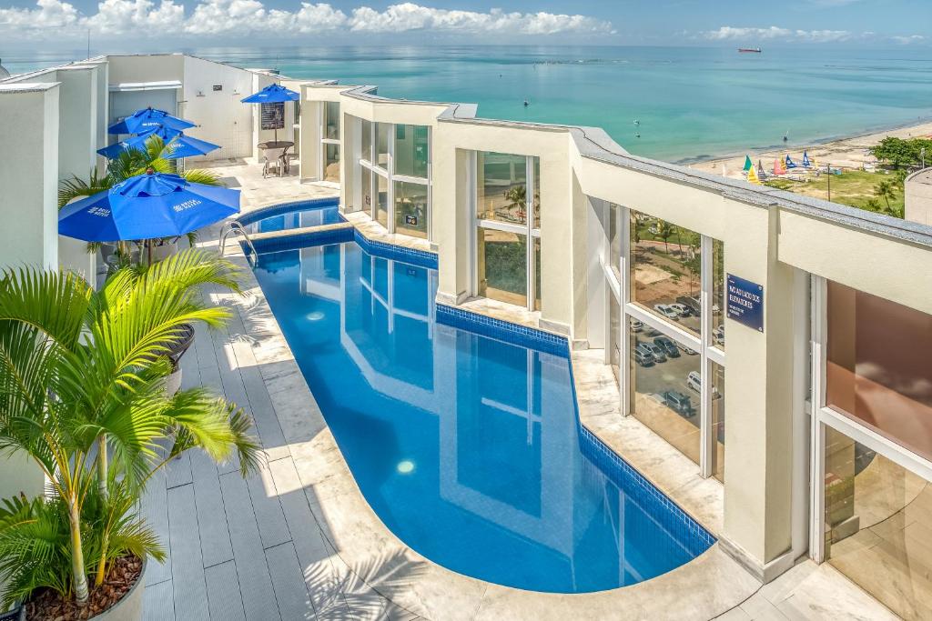 Piscina do Hotel Brisa, em Alagoas, com paredes altas de vidro no lado direito, e vista da praia cristalina azulada localizada bem próxima do local