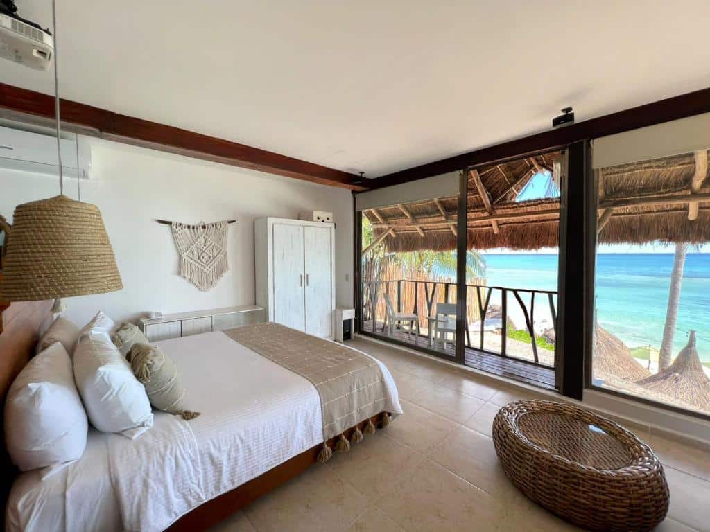 Quarto do Hotel Colibri Beach com uma cama de casal, uma varanda de frente para o mar e alguns móveis rústicos, para representar os hotéis em Playa del Carmen