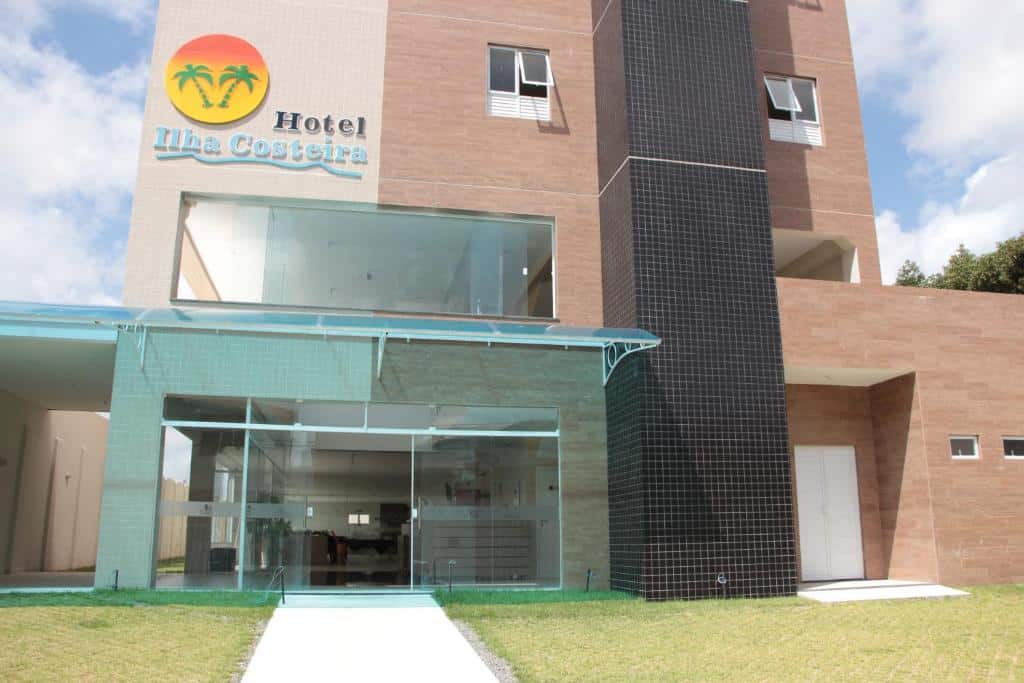 Fachada do Hotel Ilha Costeira com porta de vidro, um pequeno gramado na frente e a construção é em tons de bege e marrom, para representar hotéis em São Luís do Maranhão