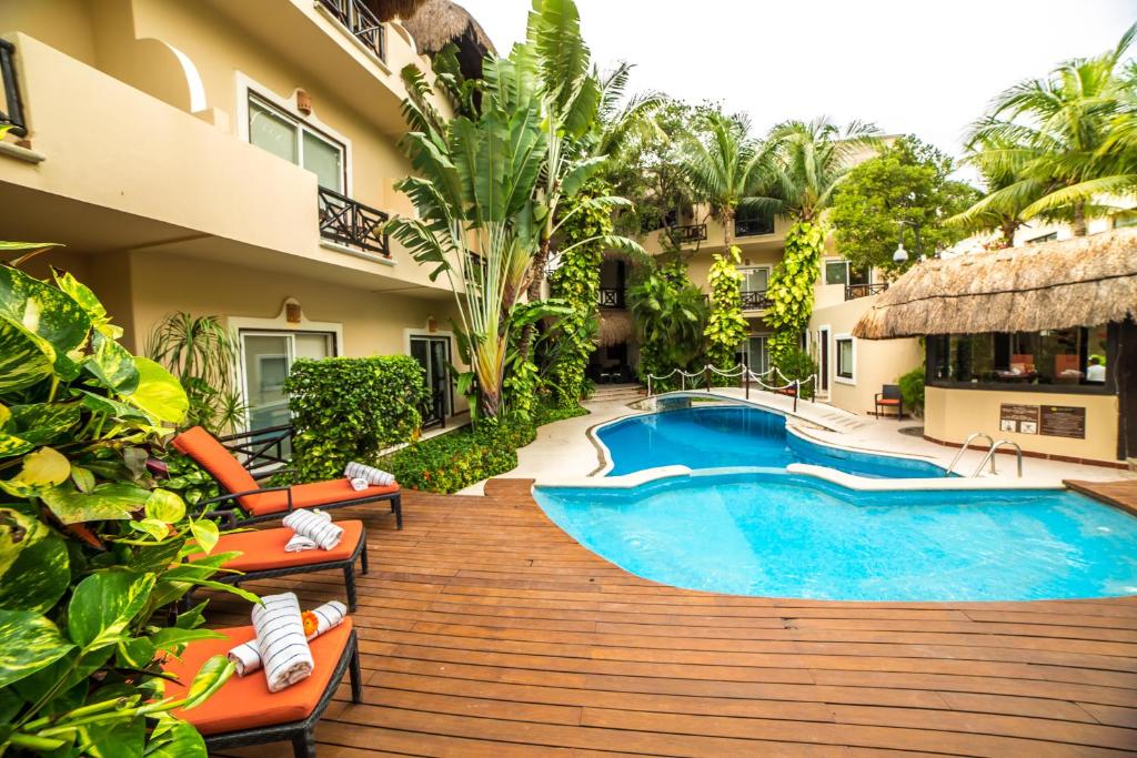 Piscina do Hotel Riviera Del Sol com um deck de madeira com espreguiçadeiras laranjas e muitas árvores ao redor