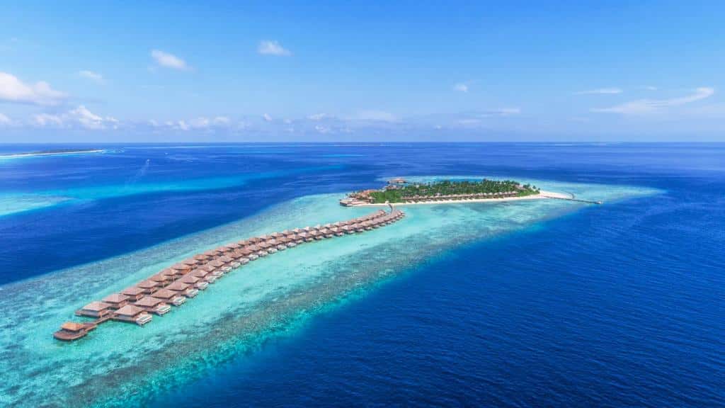 Vista aérea de uma ilha, onde fica o Hurawalhi Island Resort, com vários chalés flutuantes no meio do mar e um mar azul turquesa em volta.