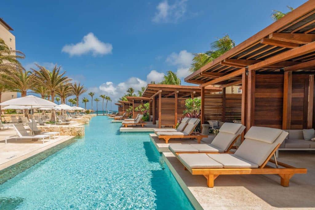 piscina do Hyatt Regency Aruba Resort & Casino com espreguiçadeiras estofadas ao redor e um céu azul ao fundo