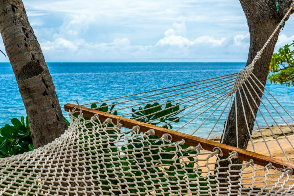 vista  a partir de uma rede trançada na praia, de águas azuis com céu claro com nuvens na Ilha Malolo, para ilustrar o post de chip celular Fiji
