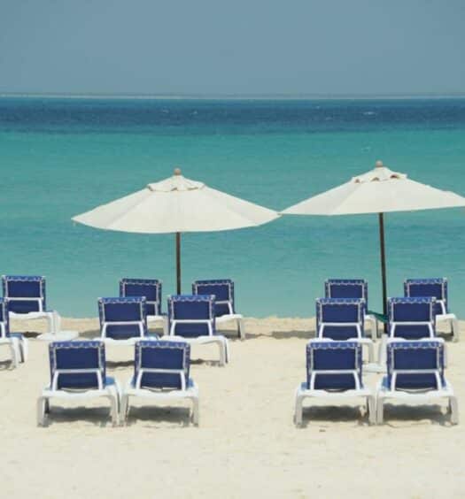 Diversas espreguiçadeiras azuis dispostas em uma areia branca da praia de frente para o mar, para representar hotéis em Isla Mujeres
