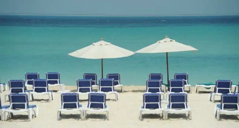 Diversas espreguiçadeiras azuis dispostas em uma areia branca da praia de frente para o mar no Ixchel Beach Hotel, um dos hotéis em Isla Mujeres.