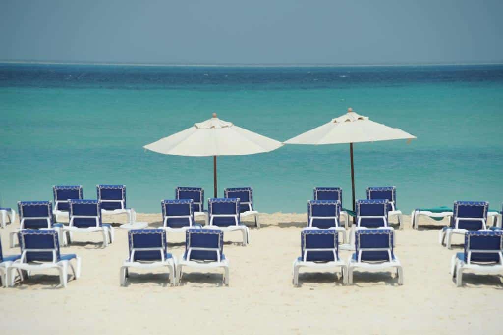 Diversas espreguiçadeiras azuis dispostas em uma areia branca da praia de frente para o mar, para representar hotéis em Isla Mujeres