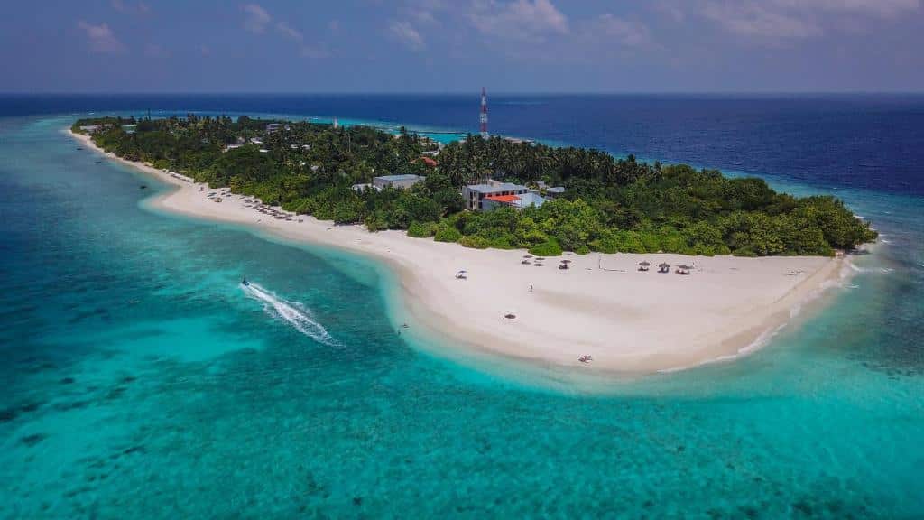 Ilha onde fica a La Palma Villa, um dos hotéis em Maldivas. O local é banhado por um mar azul cristalino e tem areia branca na costa. O prédio do hotel fica no meio, rodeado por árvores verdes.