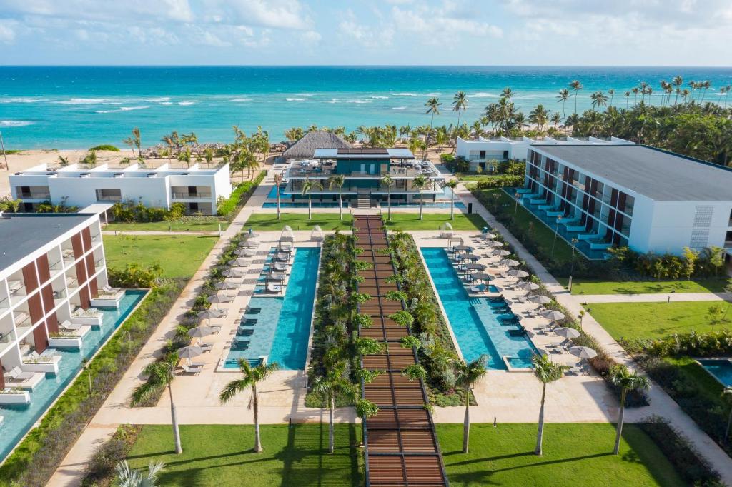 Vista aérea do Live Aqua Beach Resort Punta Cana, mostrando as piscinas do local, com várias espreguiçadeiras e árvores em volta, além dos prédios com varanda e piscina privativa nos quartos. Há também, ao fundo da foto, o mar com poucas ondas. num tom azulado cristalino durante um dia ensolarado
