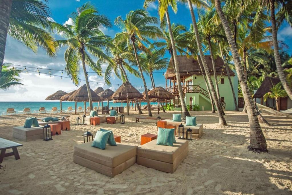 Diversos pequenos sofás com almofadas dispostos na areia da praia em frente ao Mahekal Beach Front Resort & Spa com alguns coqueiros ao redor