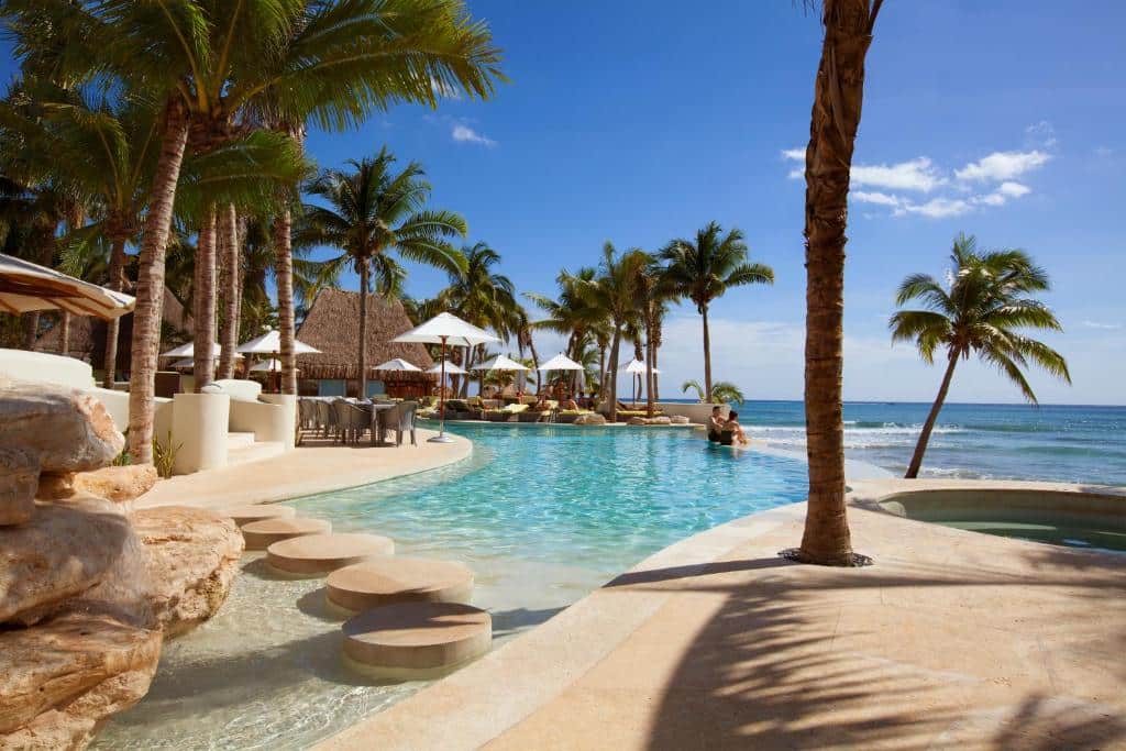 Piscina do Mahekal Beach Front Resort & Spa de frente para a praia com muitos coqueiros ao redor