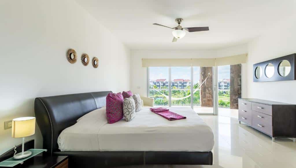Quarto do Mareazul Beach Front Resort Playa del Carmen com uma sacada ampla com rede e vista para um jardim, dentro há uma cama espaçosa de casal com almofadas, além de um ventilador de teto e uma cômoda