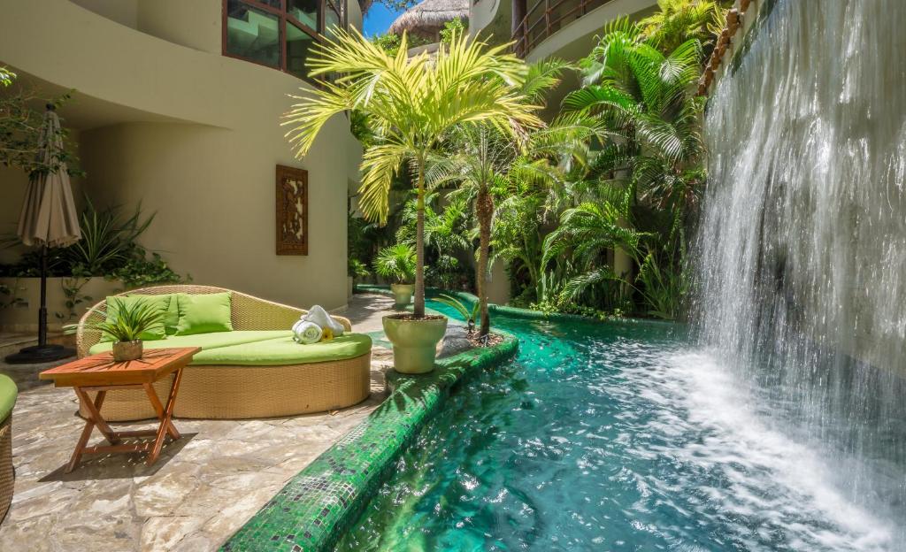 Uma piscina com uma pequena queda-d'água de frente para a varanda de um dos quartos do Maya Villa Condo Hotel and Beachclub com alguns coqueiros e plantas ao redor
