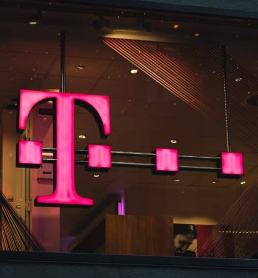 logo da T-Mobile pendurado numa loja, demonstrado pela letra T na cor rosa, com quatro pontos sobrepostos à letra.