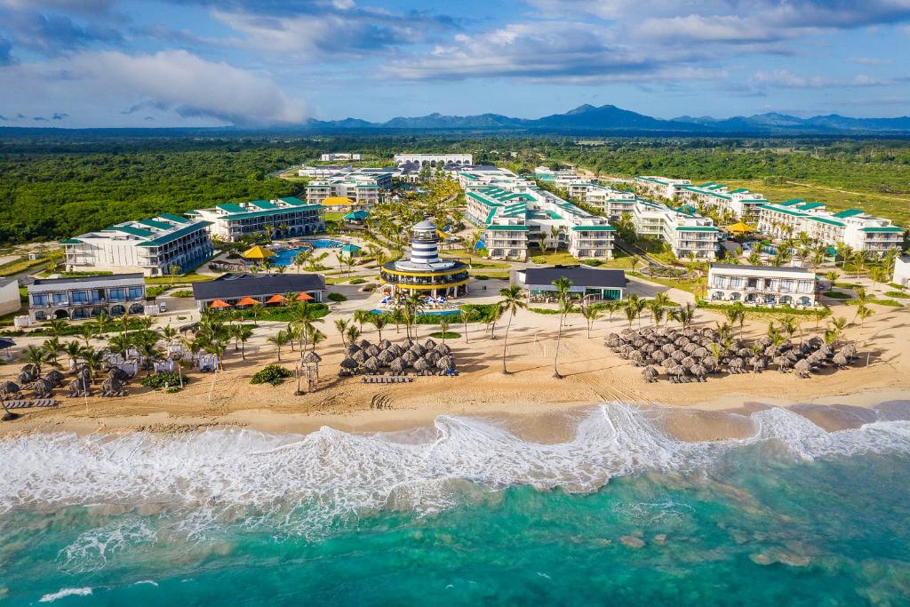 Complexo do Ocean el Faro Resort, com vista aérea de vários prédios em diferentes tamanhos do resort, piscinas, bastante natureza verde em volta, espreguiçadeiras na areia fofa e mar com água cristalina num tom azul turquesa.