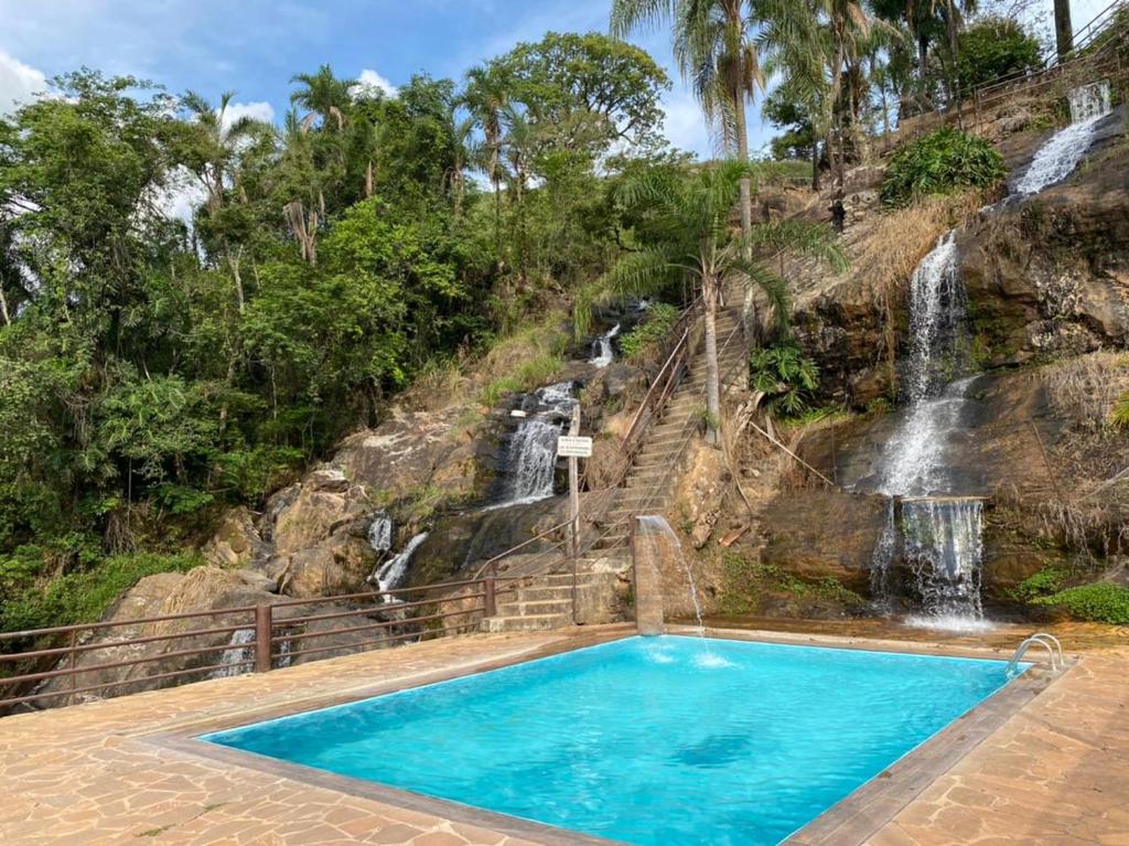Vista da piscina do Pousada Cachoeira Dos Sonhos durante o dia, no fundo uma queda de água parece uma pequena cachoeira. Representa chalés em Serra Negra.