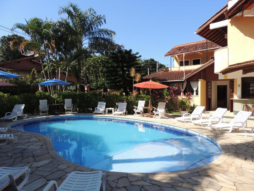 Vista da piscina da Pousada Mosaico Brasil durante o dia com cadeiras em volta e a hospedagem do lado esquerdo.