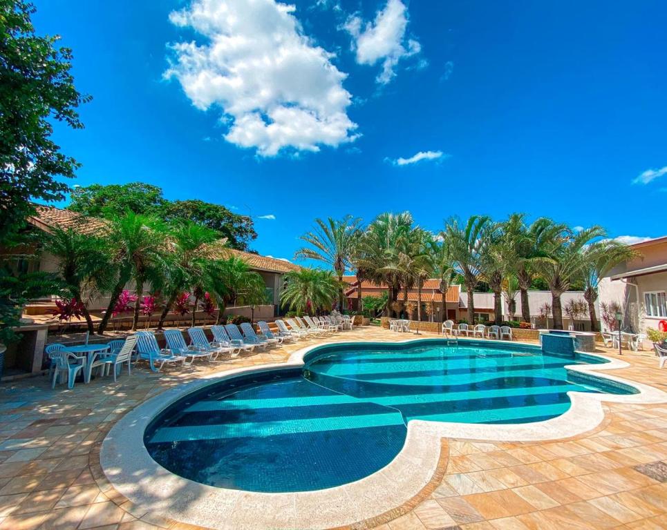 Vista da piscina do Villa de Holanda Parque Hotel durante o dia com cadeiras perto da piscina e com coqueiros atrás das cadeiras. Representa hotéis em Holambra