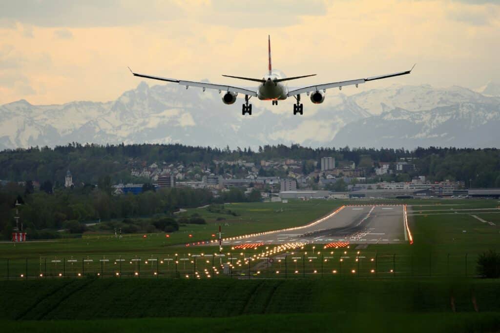 Avião pousando na pista do Aeroporto em Zurique, na Suíça, com luzes iluminando o caminho e vista da cidade ao fundo, ilustrando o post sobre o ETIAS